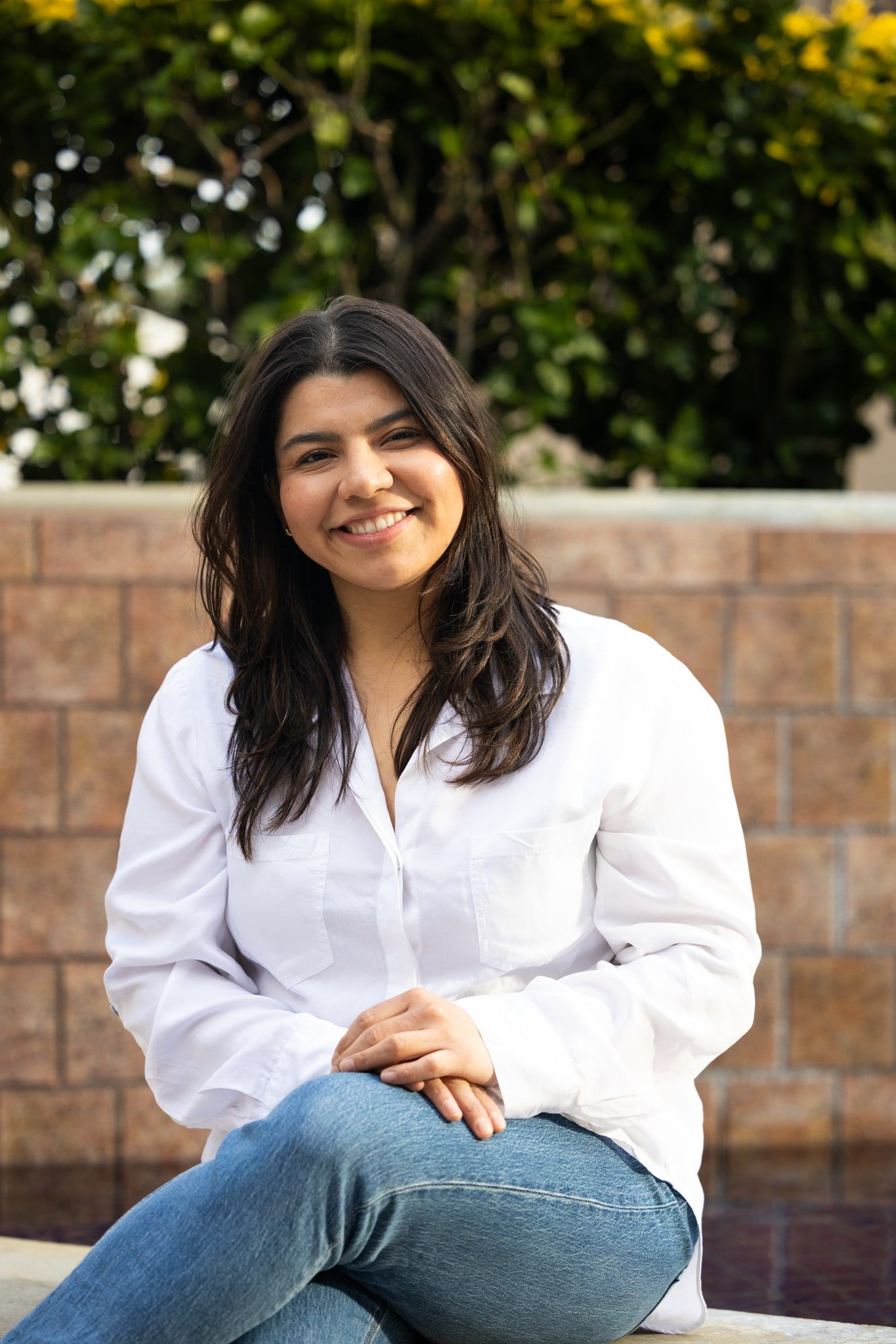 Kimberly Ramirez seated outdoors in a white shirt, smiling at the camera